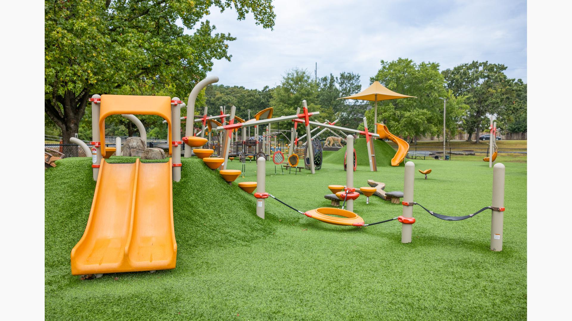 A large open space with artificial grass filled with different playground structures and activities.
