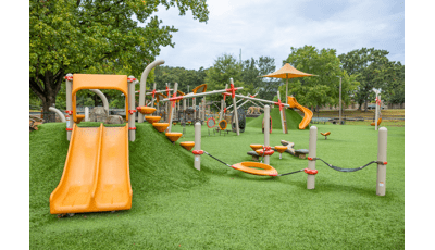 A large open space with artificial grass filled with different playground structures and activities.