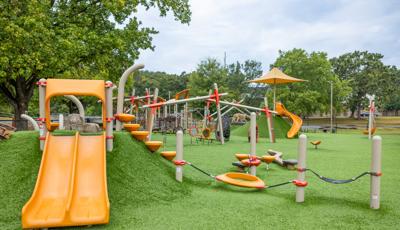 A large open space with artificial grass filled with different playground structures and activities.