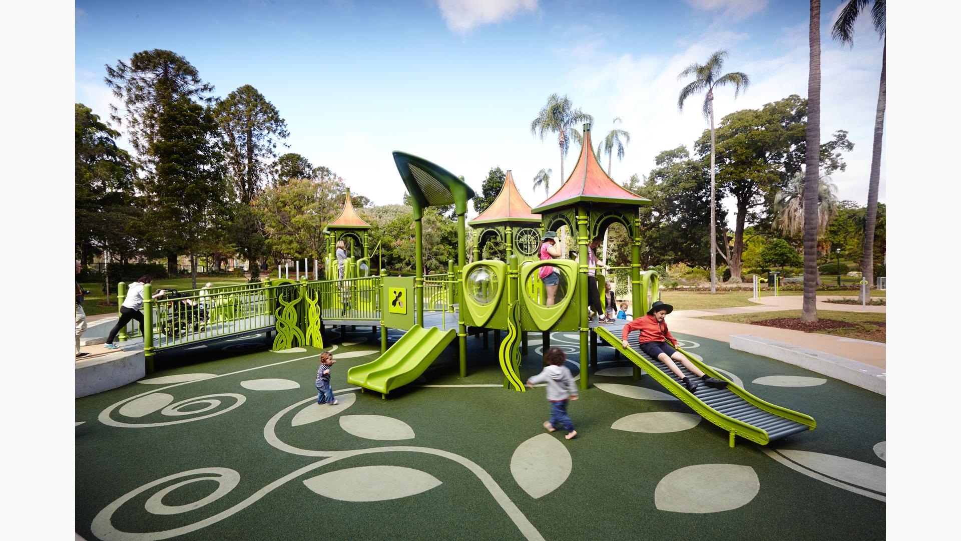 Children play on a custom all green inclusive nature themed playground with ramps and grass blade accent designs. 
