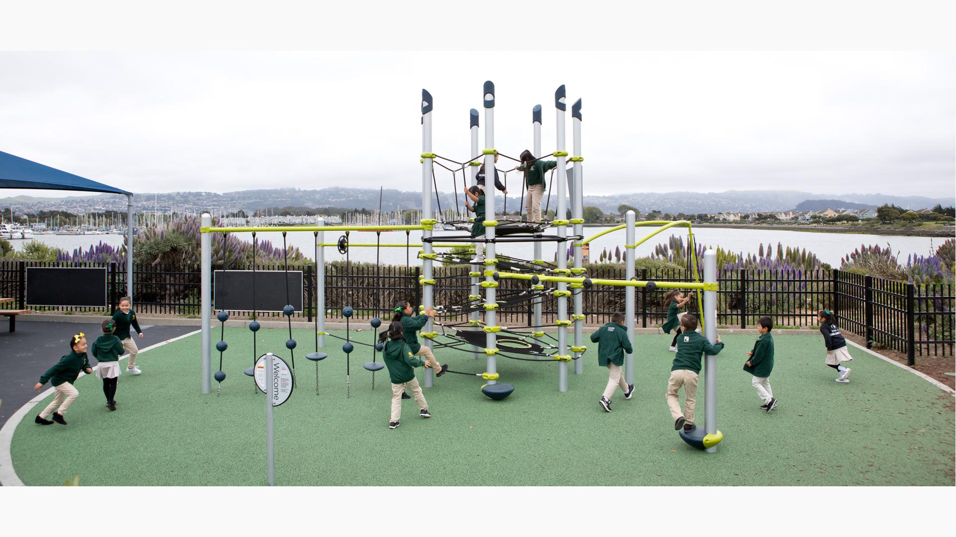 Kids dressed in the school uniforms play all over a tower structure with additional climbers, spinners, and other playground activities.
