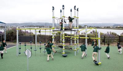 Kids dressed in the school uniforms play all over a tower structure with additional climbers, spinners, and other playground activities.