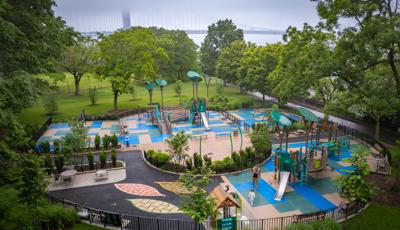 Elevated view of a park playground surrounded by large trees and a river front nearby.