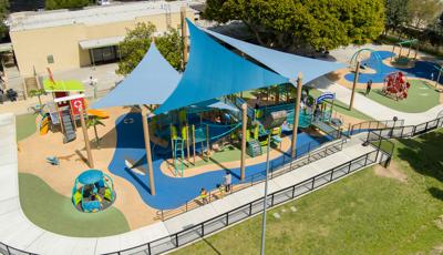 Elevated view of large blue triangle shade sails over a large inclusive beach themed playground. 