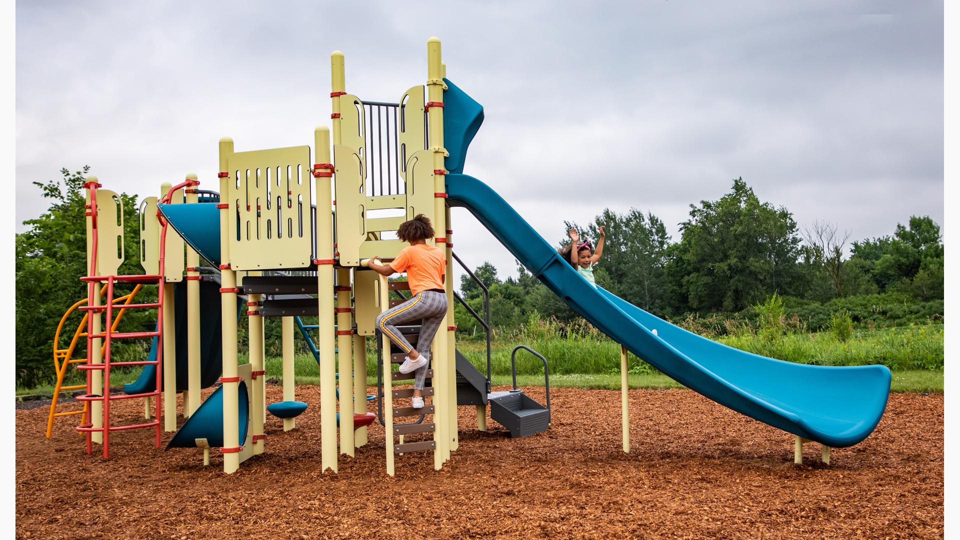 A girl puts her hands in the air as she slides down a blue Alpine Slide on a pale yellow PlayBooster playset.