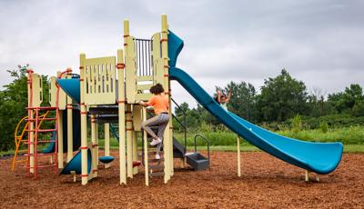 A girl puts her hands in the air as she slides down a blue Alpine Slide on a pale yellow PlayBooster playset.