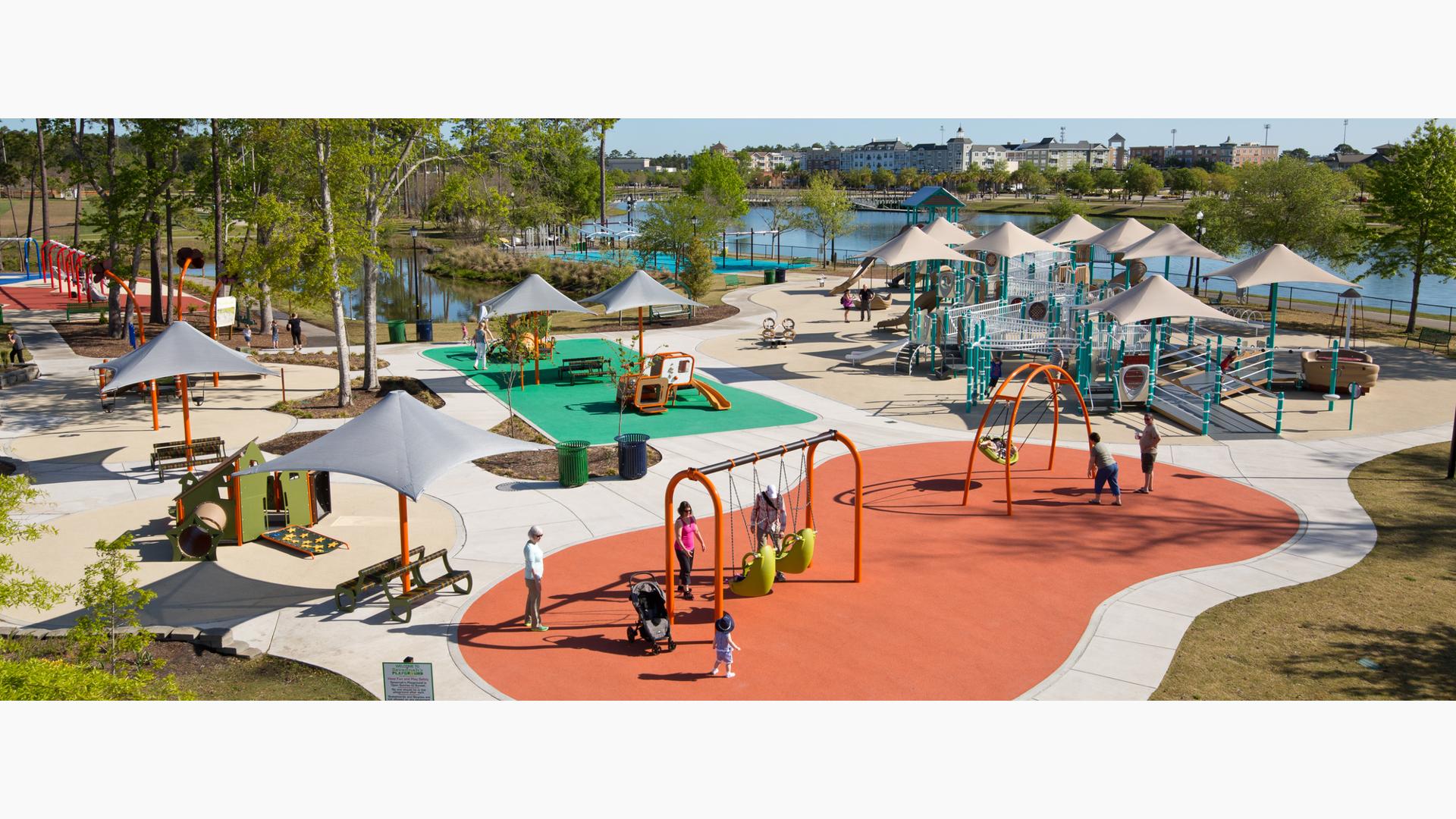 Parents push their kids on swings at Savannah's Playground. The PlayBooster play structure comes with shade sails and loads of ramps for all kids to access.