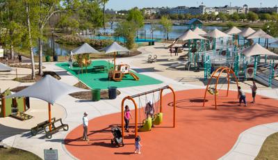 Parents push their kids on swings at Savannah's Playground. The PlayBooster play structure comes with shade sails and loads of ramps for all kids to access.