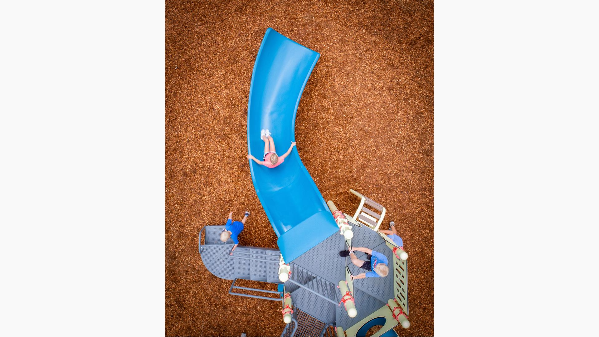 Aerial view of a perforated metal play structure with a child descending a blue Alpine Slide.