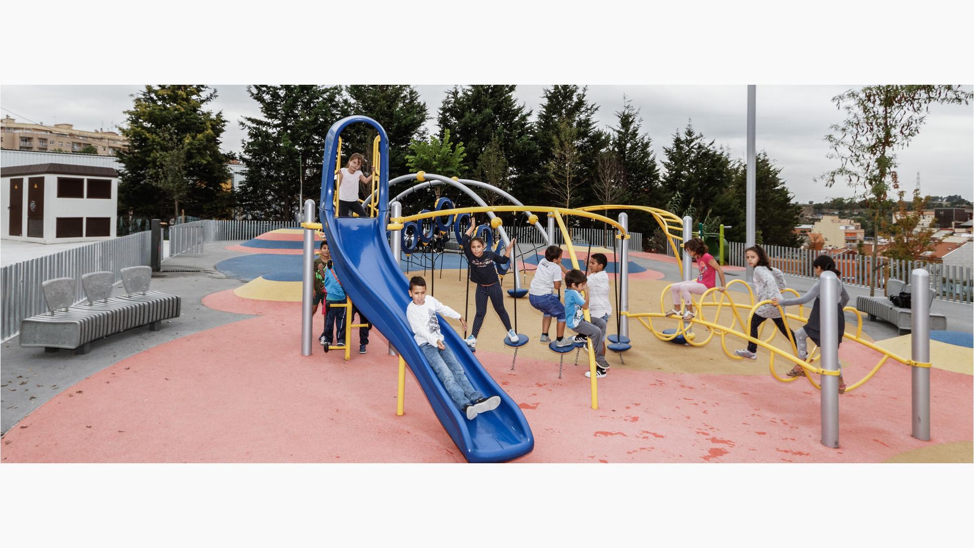 Boy riding down Evos slide, with line forming behind him. Other kids play on the Disc Challenge and Ring Tangle Climber.