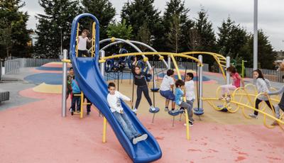 Boy riding down Evos slide, with line forming behind him. Other kids play on the Disc Challenge and Ring Tangle Climber.