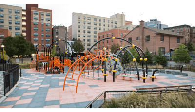 Black arched playground posts make up the framework of play structures at a city playground with black and orange square safety surfacing.