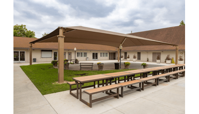 A center court yard with large brown rectangular shade pavilion with a row of picnic tables on one side.
