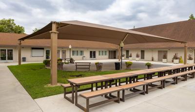 A center court yard with large brown rectangular shade pavilion with a row of picnic tables on one side.