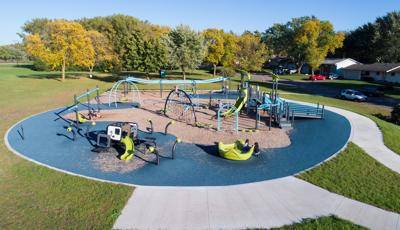 Surrounded by trees, across the street from a neighborhood. Goodrich Park features an abundance of activities for kids f all ages and abilities. The ground is a combination of sand and a manufactured surface.