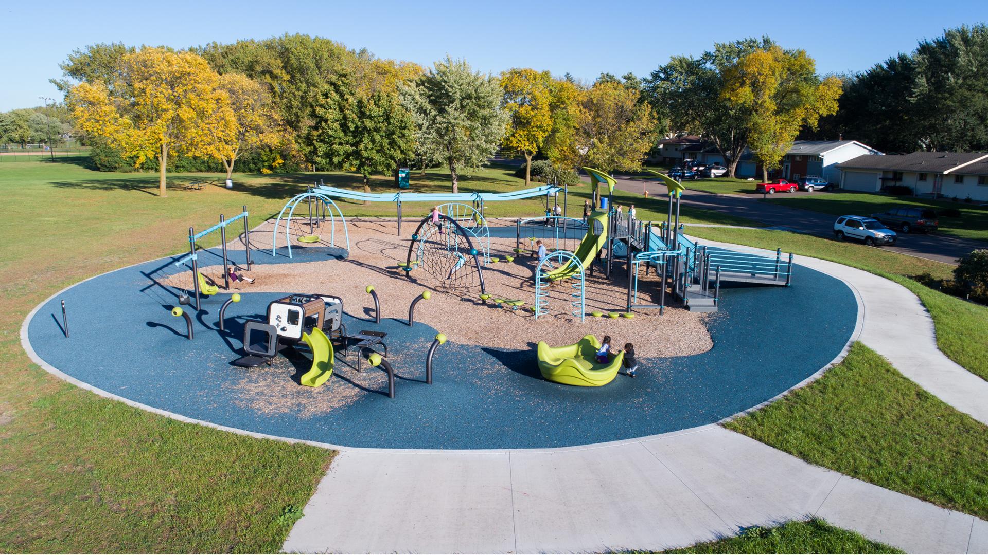 Surrounded by trees, across the street from a neighborhood. Goodrich Park features an abundance of activities for kids f all ages and abilities. The ground is a combination of sand and a manufactured surface.