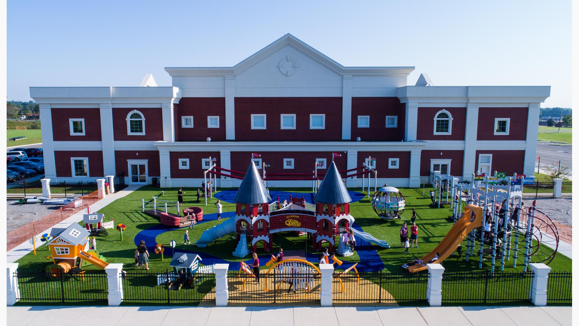 School children wearing school uniforms play on castle-themed playground structure. Childcare-aged children play on three playhouse structures colored red, tangerine and blue. 