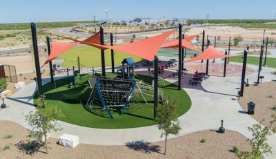 Elevated view of large orange triangular shade sails covering a circular play area with artificial grass and three separate structures to play on.