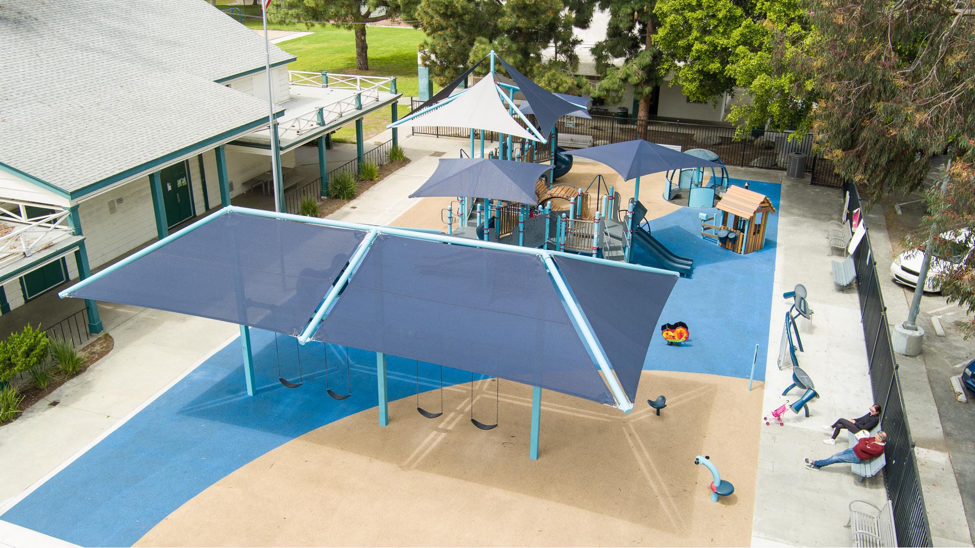 Multiple shade structures cover one large playground surrounded by a inclusive carousel ride, play house, outdoor musical instruments station, and swing set.