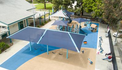 Multiple shade structures cover one large playground surrounded by a inclusive carousel ride, play house, outdoor musical instruments station, and swing set.