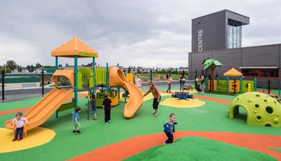 Children play at a fenced in play area next to a building. Two separate play areas are separated by a fence one area for older children and the other for younger kids. 