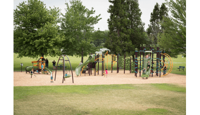 Families play at a park playground with play structures that have unique rope disc and geometric climbers, younger age appropriate play structures and a inclusive large disc swing.