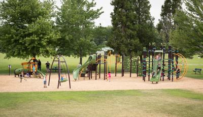 Families play at a park playground with play structures that have unique rope disc and geometric climbers, younger age appropriate play structures and a inclusive large disc swing.