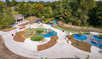 Aerial image of playground site which includes several play areas for kids of all ages. For smaller kids there are two play house themed playstructures. And for older kids there is a nature themed playground with accessible ramps. 