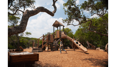 Girl riding down slide as friend in grey crosses playground. Play-naturally themed, Ponce Preserve sits in the natural lay of the of the Florida landscape.