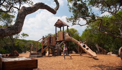 Girl riding down slide as friend in grey crosses playground. Play-naturally themed, Ponce Preserve sits in the natural lay of the of the Florida landscape.