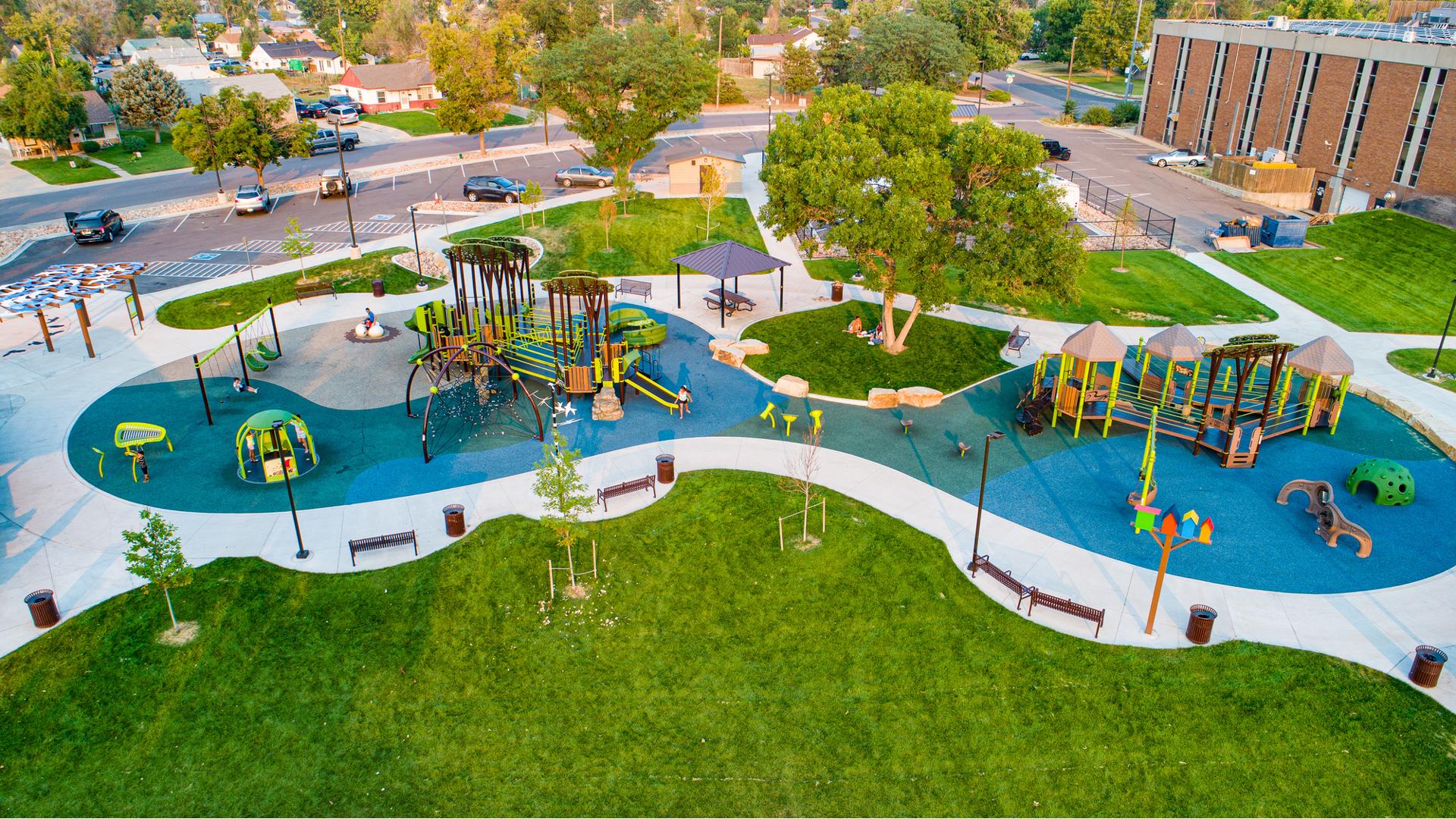 Full elevated view of a large inclusive play area with two separate nature themed play structures surrounded by additional play activities like swing sets, climbers, and outdoor musical instruments.