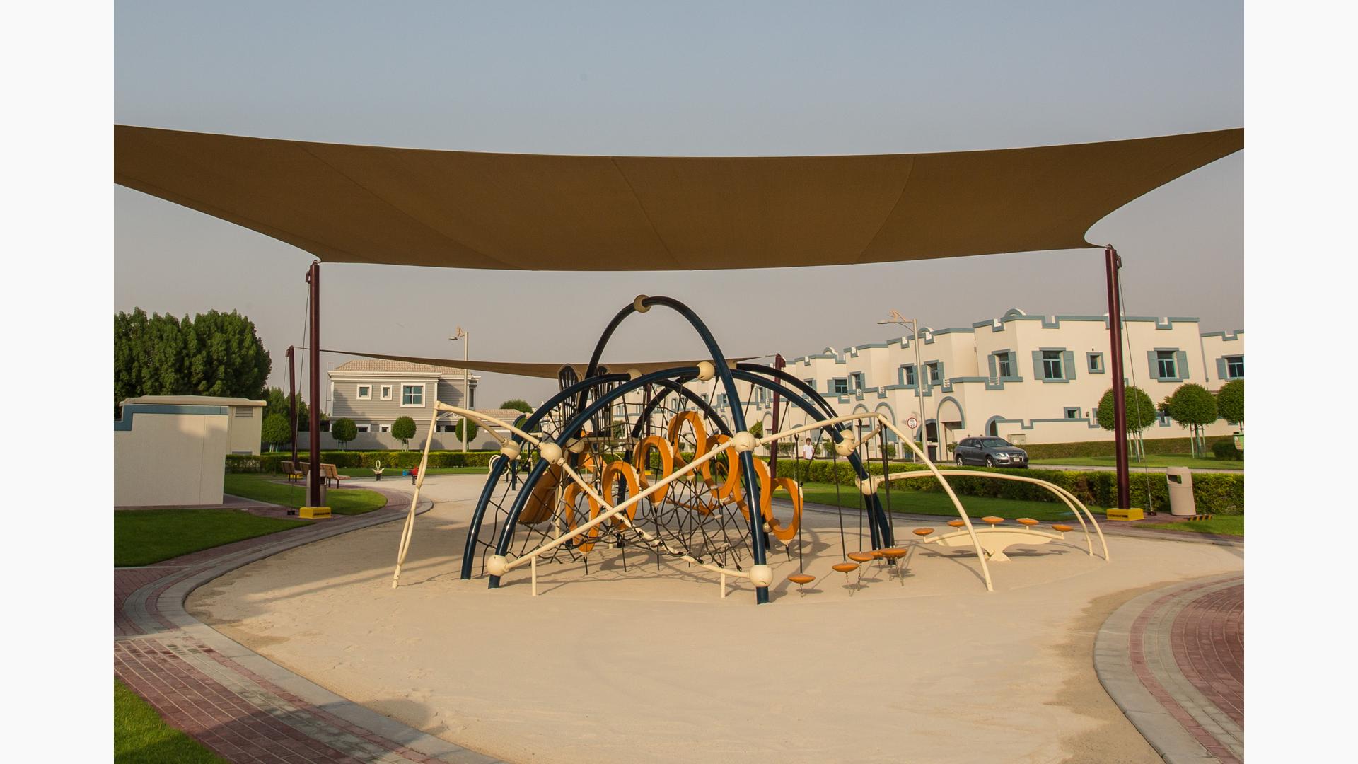 Under SkyWays shade canopy this Evos play structure sitting in  a sand playground. Freestanding riders in the distance.
