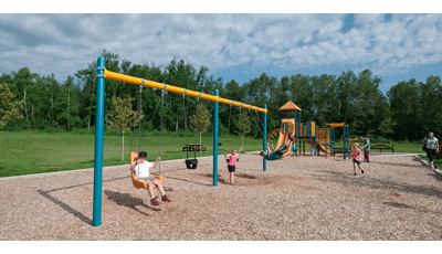 Some kids playing on the swings as others frolic on the play structure.