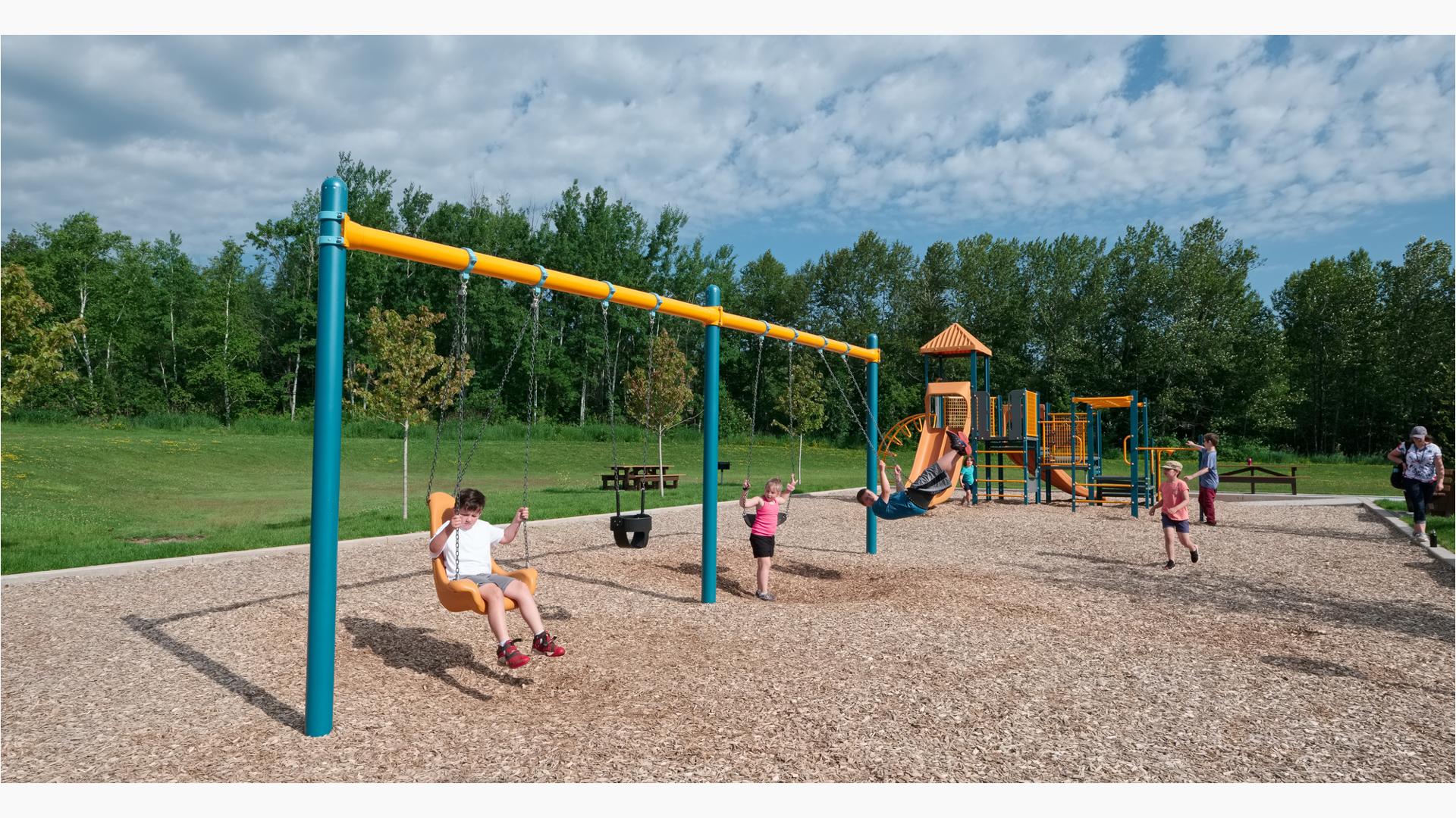 Some kids playing on the swings as others frolic on the play structure.