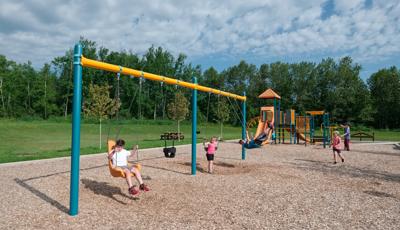 Some kids playing on the swings as others frolic on the play structure.