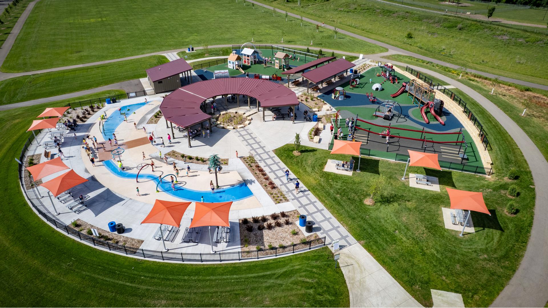 Elevated view of a park playground with a train and historical building theme with a splash pad also connected.