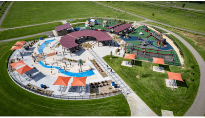 Elevated view of a park playground with a train and historical building theme with a splash pad also connected.