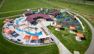 Elevated view of a park playground with a train and historical building theme with a splash pad also connected.