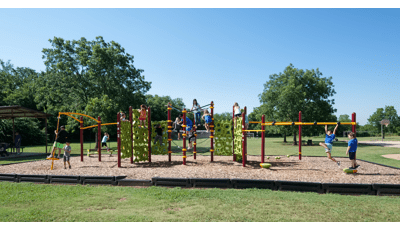 School-aged kids play on their school playground with green geometric shaped-like climbers. Playground also includes monkey bars, spinner and tight-rope play event. 