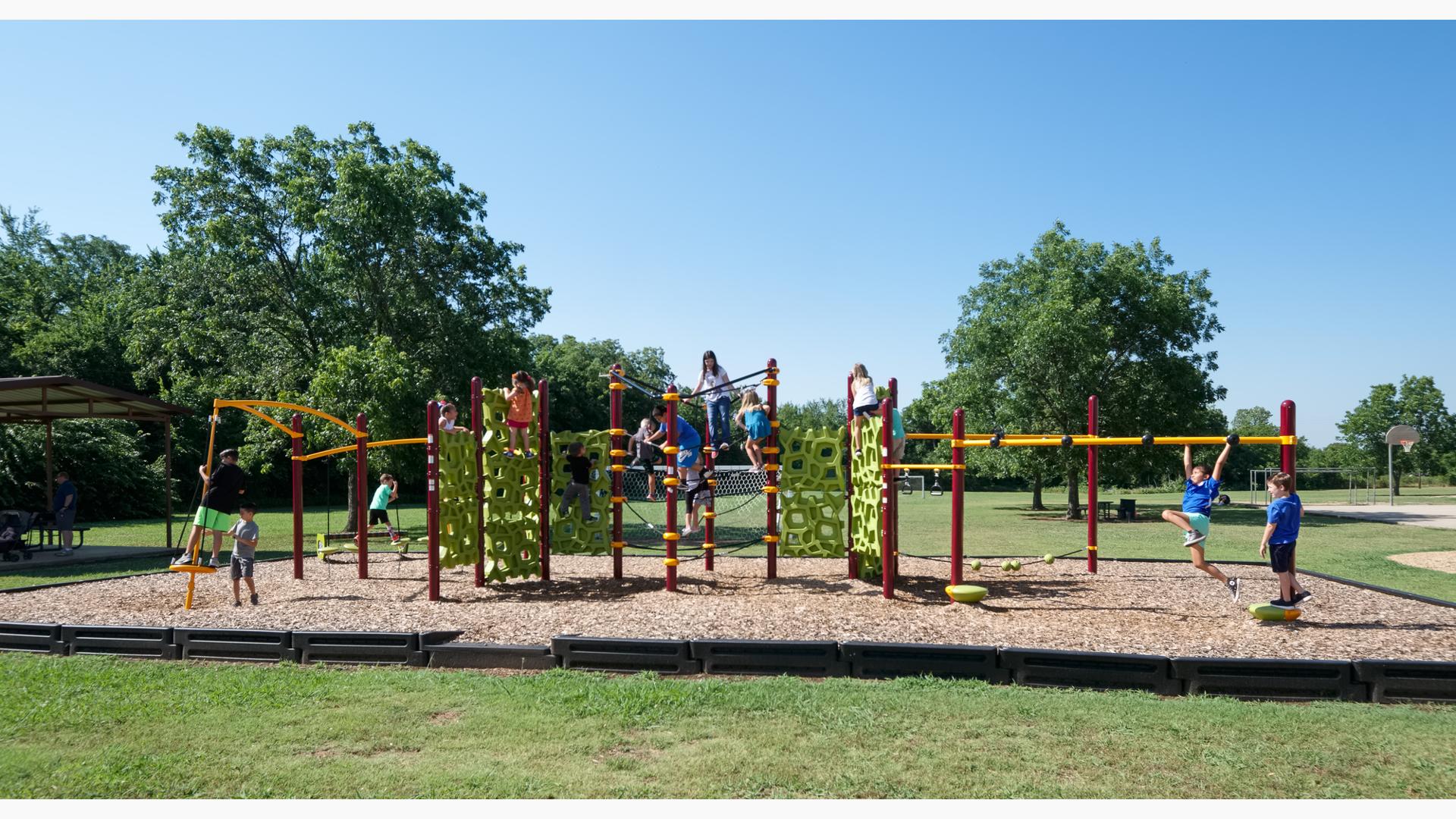 School-aged kids play on their school playground with green geometric shaped-like climbers. Playground also includes monkey bars, spinner and tight-rope play event. 