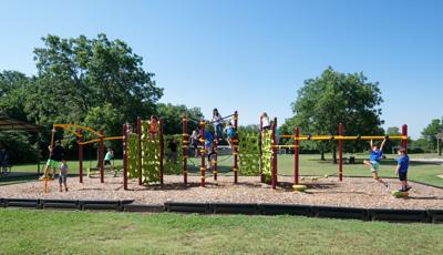School-aged kids play on their school playground with green geometric shaped-like climbers. Playground also includes monkey bars, spinner and tight-rope play event. 