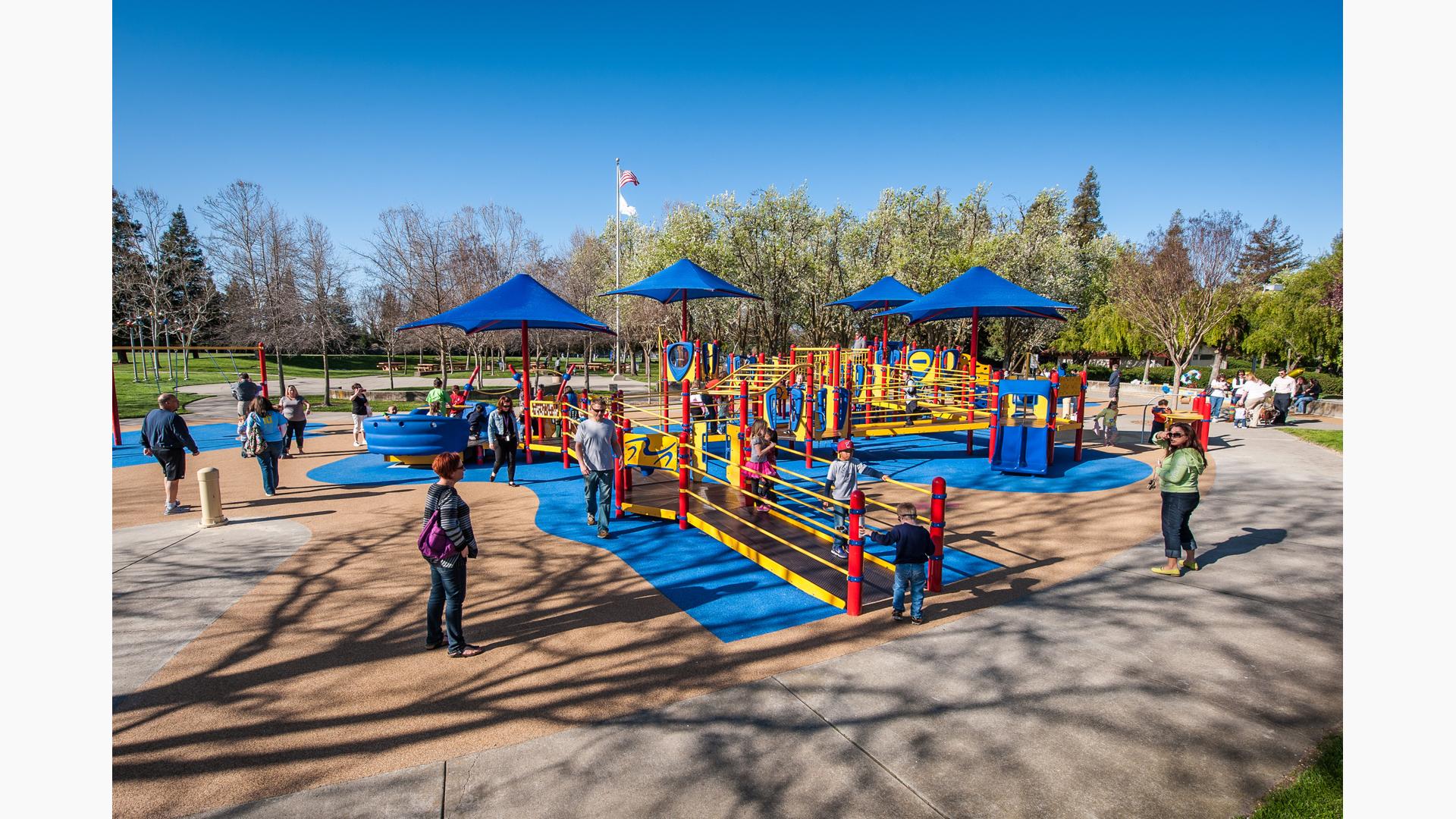 Families playing on primary colored fully-ramped accessible inclusive playground.