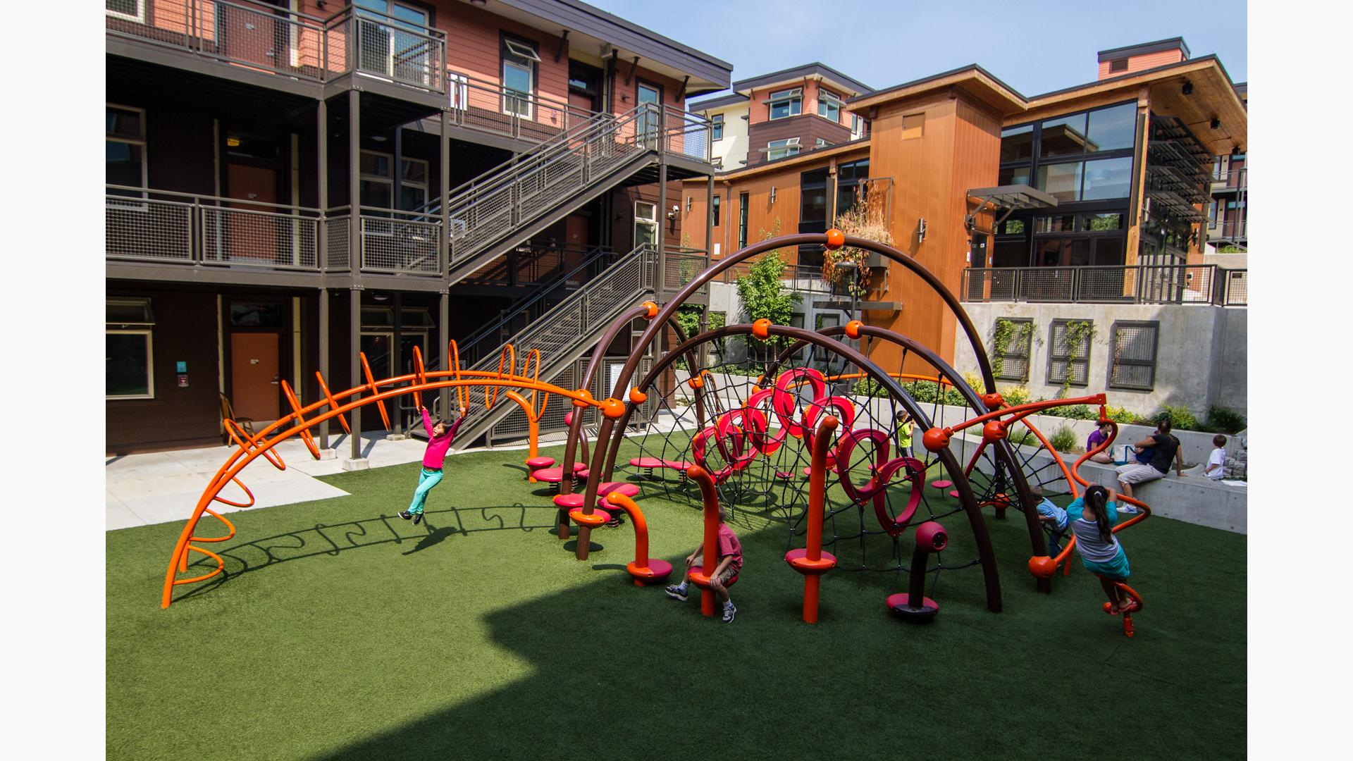 School aged kids playing in geometric playground with  brown complex building in the background. 