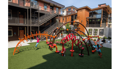 School aged kids playing in geometric playground with  brown complex building in the background. 