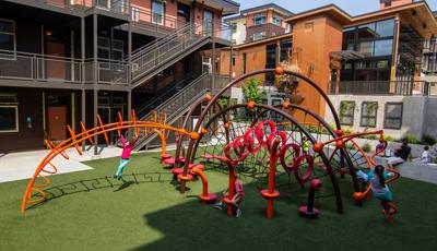 School aged kids playing in geometric playground with  brown complex building in the background. 