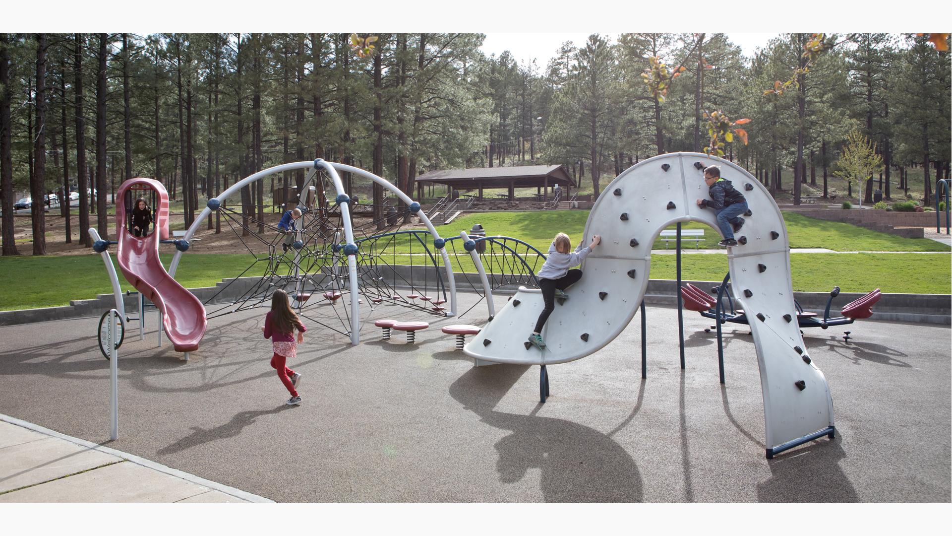 Girl in red running toward Evos slide. Two children play on climbing structure and a boy sits at the top of a net eclipse.