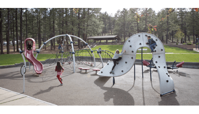 Girl in red running toward Evos slide. Two children play on climbing structure and a boy sits at the top of a net eclipse.