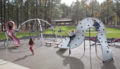 Girl in red running toward Evos slide. Two children play on climbing structure and a boy sits at the top of a net eclipse.