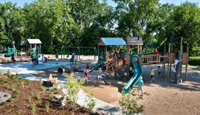 Families play on a nature and treehouse themed playground structures with log climbers and logging themed activities.