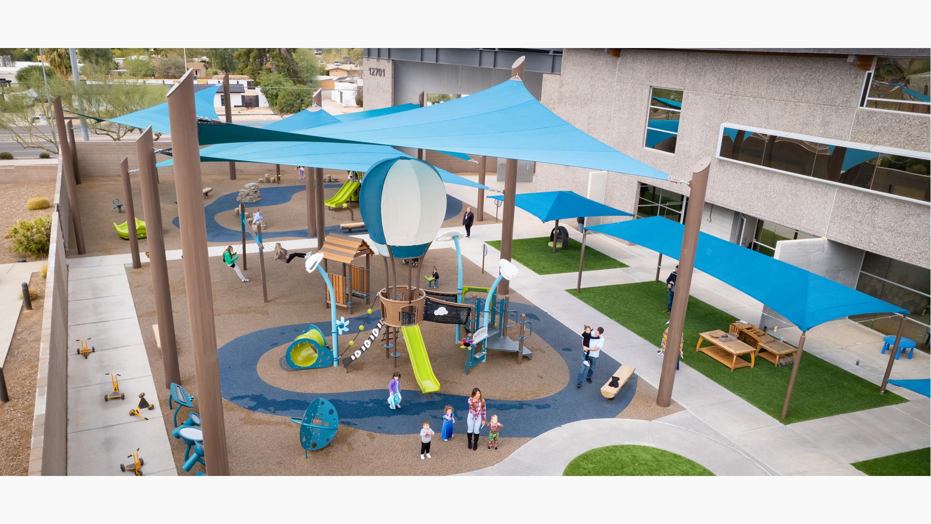 Elevated view of large blue shade sails or a playground area next to a building.